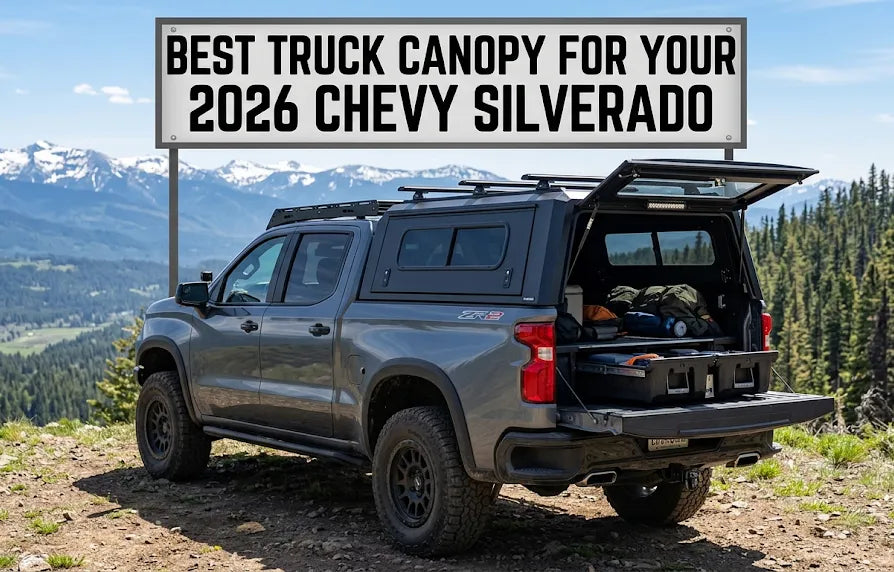 A gray Chevy Silverado truck parked in a mountainous area with a black truck canopy installed, featuring a banner that reads "BEST TRUCK CANOPY FOR YOUR 2026 CHEVY SILVERADO."