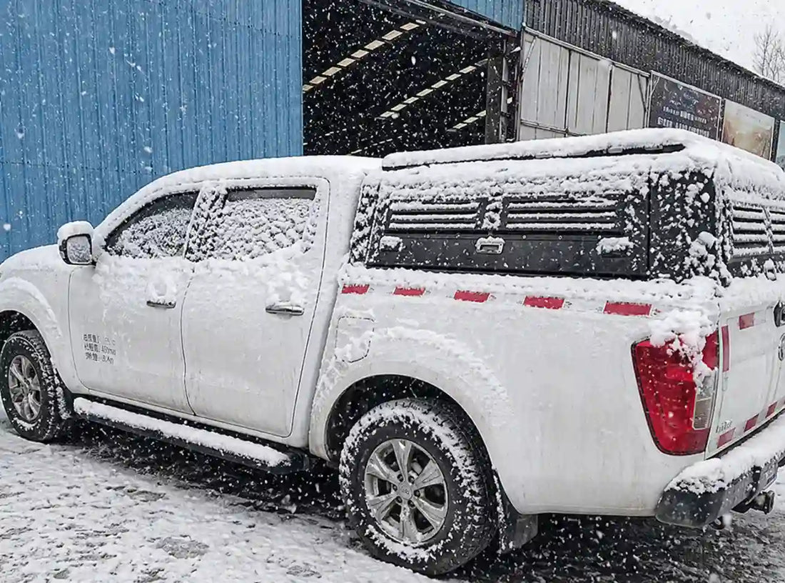 ArmaCap heavy-duty manganese steel truck canopy on a white pickup truck, heavily covered in snow, demonstrating extreme weather durability and structural strength under heavy snow loads.
