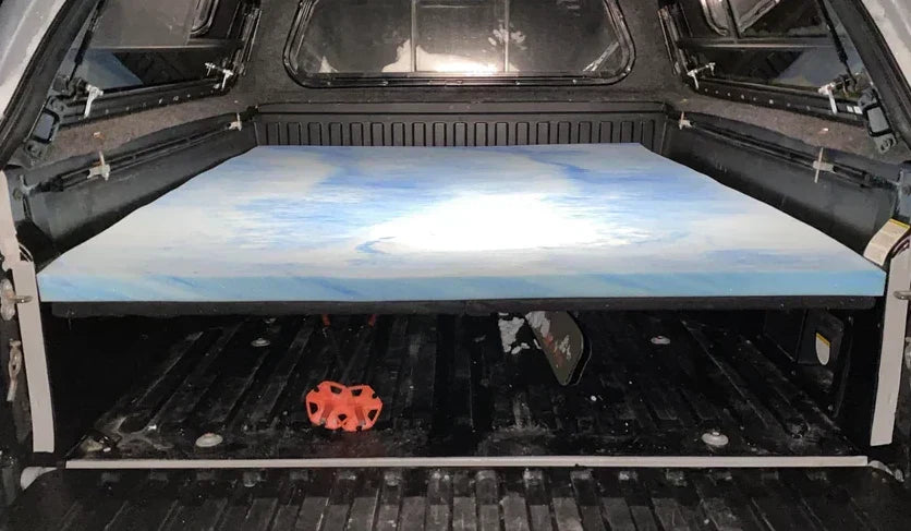 Interior view of a Tacoma overlanding setup, showing a simple DIY bed platform made of 2x6 supports and carpeted plywood.